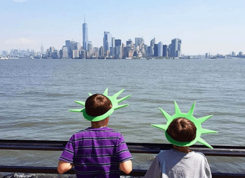 two children looking over the Hudson river wearing Statue of Liberty hats