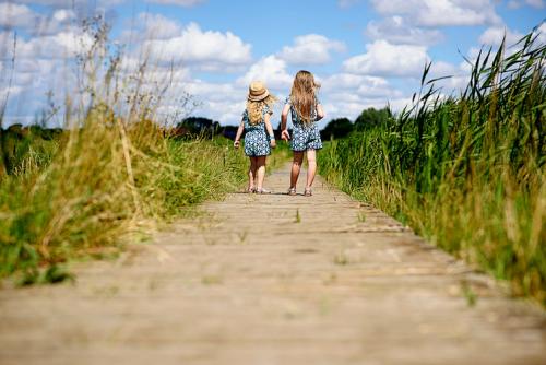Two girls walk down wooden path through a field of long grass