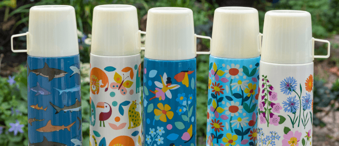 Five patterned thermos flasks in a row, against some foliage