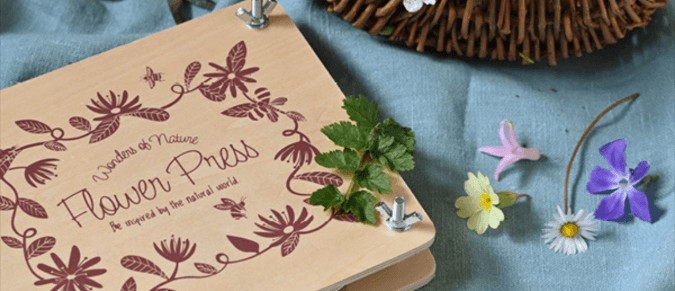 A wooden flower press on a table next to some picked flowers