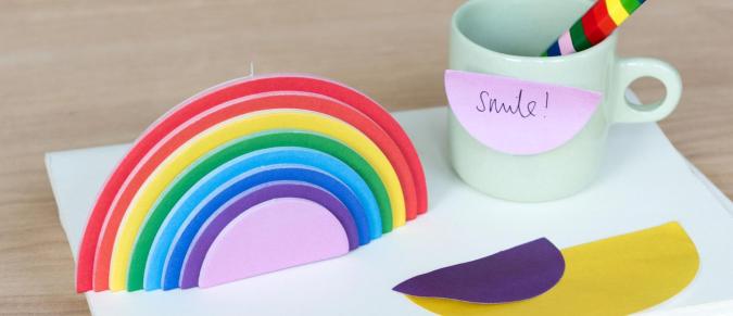 Rainbow sticky notes on a desk next to a mug with a rainbow pencil inside