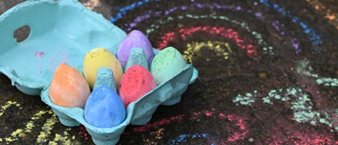 Chalk eggs in a box next to chalk drawings on the ground