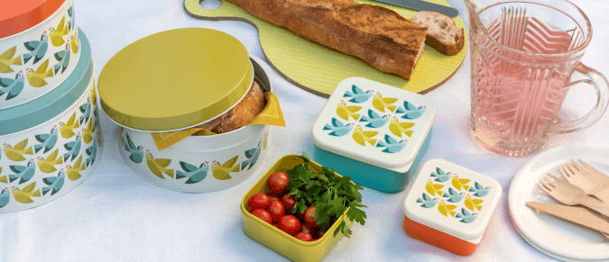 A picnic set up, including snack boxes, cake tins, bread and a jug of squash