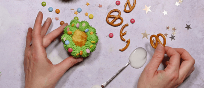 A hand holds a cupcake decorated like a Christmas tree