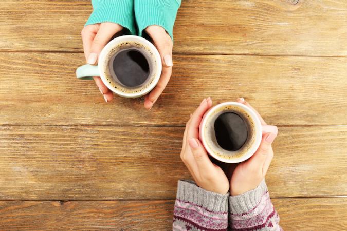 two women holding their coffee mugs across the table