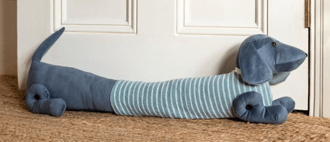 A draught excluder shaped like a sausage dog lies in front of a door