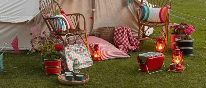 A large tent with chairs, a portable barbecue, cushions and lamps in front