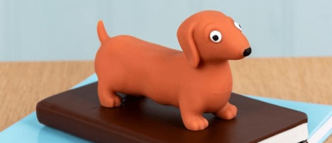 A squishy toy sausage dog sits on a brown notebook