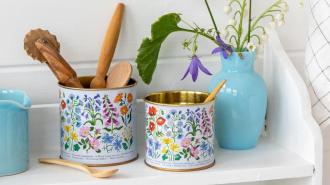 Mini storage tins on self with wooden spoons, next to vase with flowers