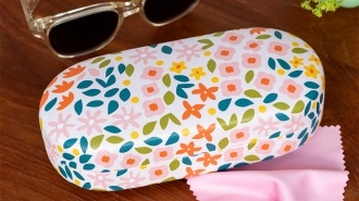 Ditsy floral-patterned sunglasses case with cleaning cloth on a wooden table.