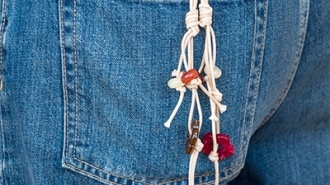 Close-up of a beaded keychain with a small red tassel and knotted cord, clipped to the back pocket of blue denim jeans.