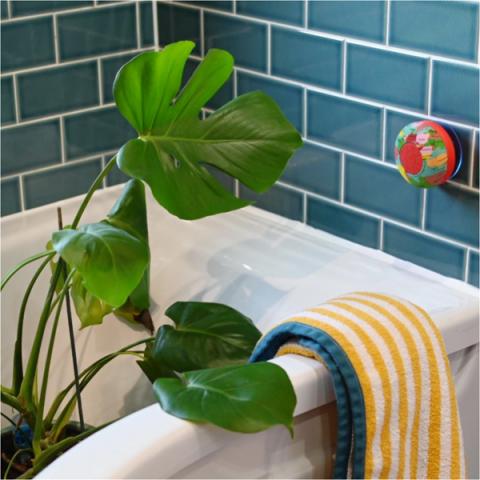 A large cheese plant in a bathtub, with a yellow stripy towel next to it