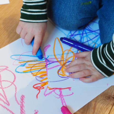 A child scribbles on a piece of paper with some crayons