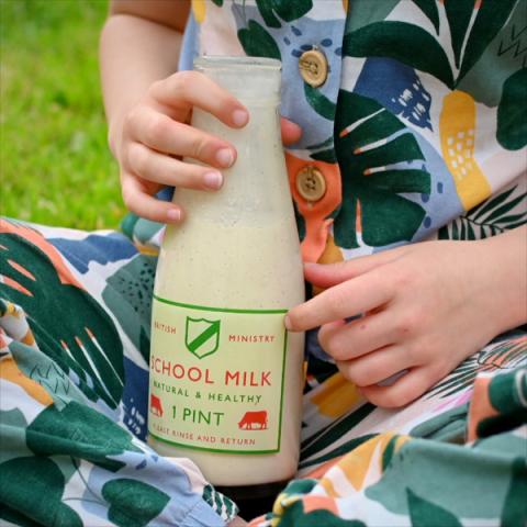 A child holds a glass bottle filled with a banana smoothie
