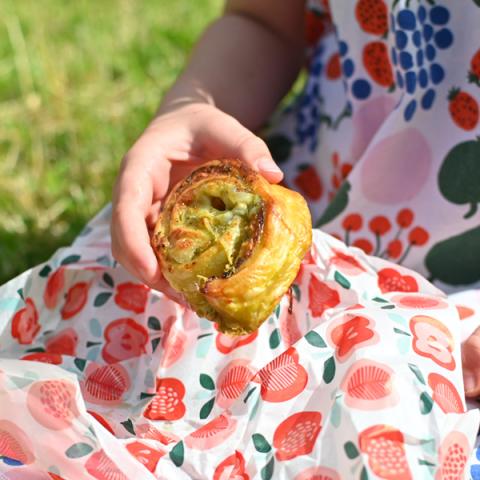 A child holds a pesto pastry roll up over a Vintage Apple print sheet of greaseproof paper