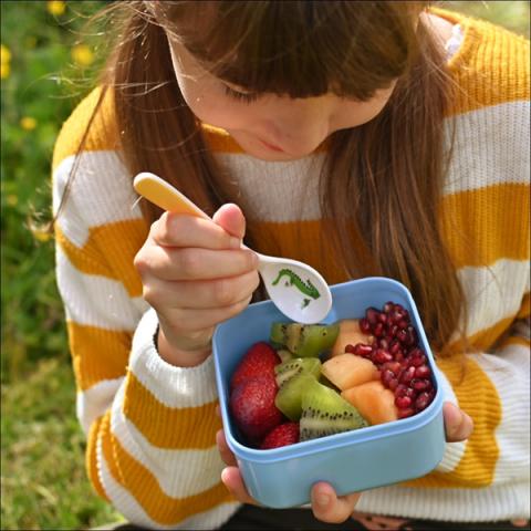 A girl holds a lunchbox filled with brightly coloured fruit