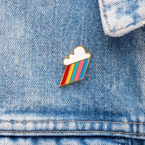 Metal cloud pin badge with rainbow rays, on a denim jacket