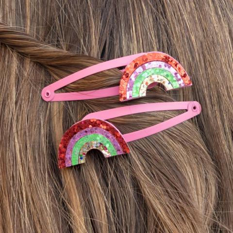 Pink hairclips with a glittery rainbow, pinned into a child's hair