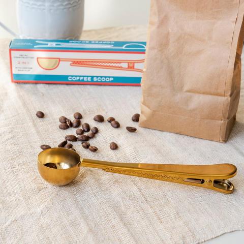 Gold coffee scoop with some coffee beans and paper bag
