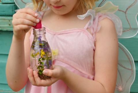 A young girl wearing fairy wings holds a glass jar filled with flowers