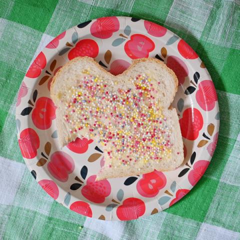 A red party plate with a slice of bread covered in hundreds and thousands