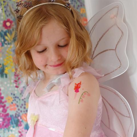 A young girl wearing fairy wings looks a temporary fairy tattoo on her shoulder