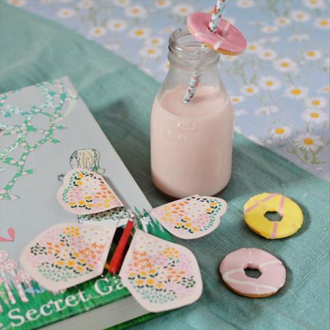 A pink paper butterfly sits on a book, next to some party rings and a jar of milk