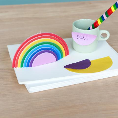 Rainbow sticky notes on a desk next to a mug with a rainbow pencil inside