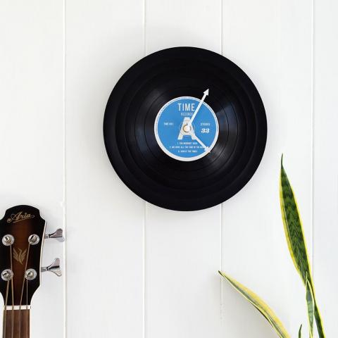 Clock shaped like a vinyl record hangs on a wall next to a guitar