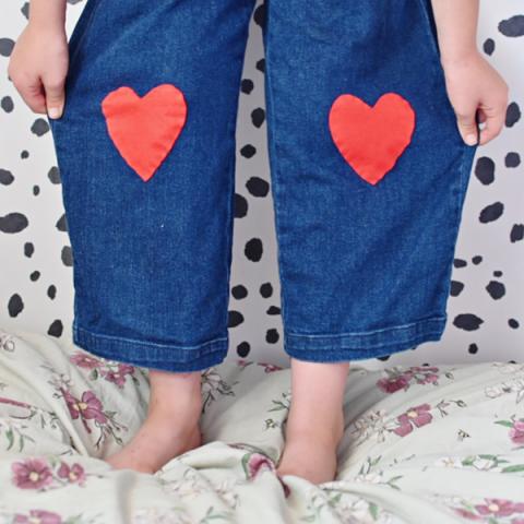 A pair of blue jeans with red heart patches on the knees
