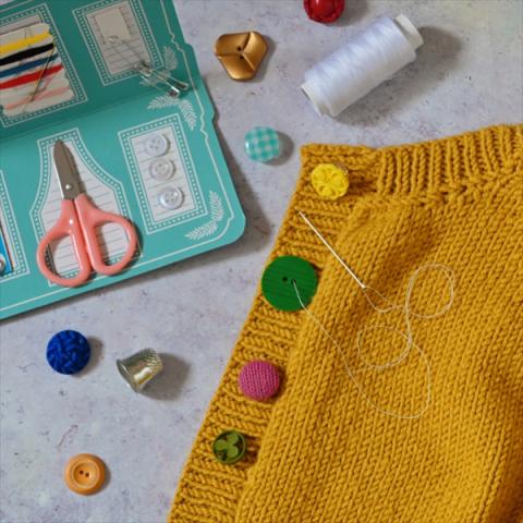 A yellow cardigan with multicoloured buttons, next to a travel sewing kit.