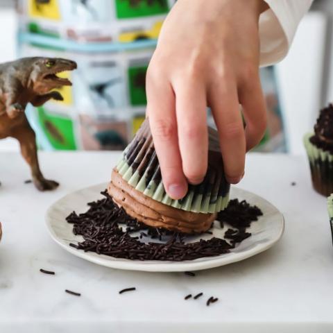 A hand holding a cupcake, rolling it in sprinkles