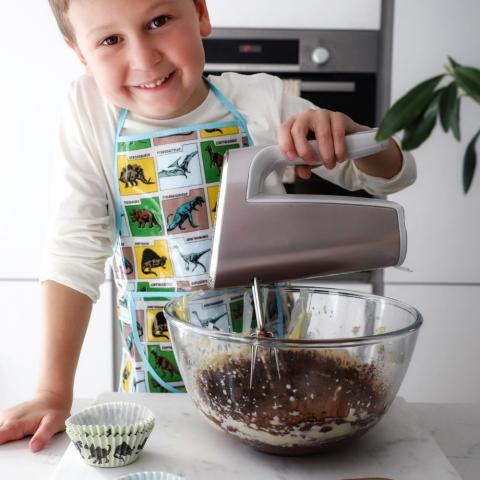 A child uses a hand mixer to make chocolate cupcake batter