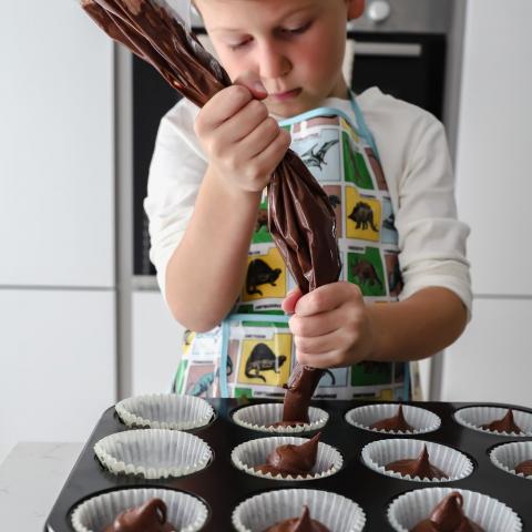 A child pipes chocolate batter into cake cases