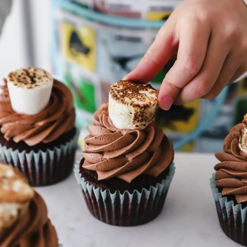A child places a toasted marshmallow on top of a chocolate cupcake