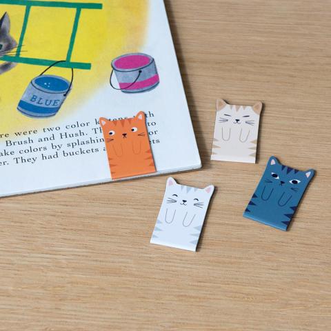 A set of magnetic cat bookmarks, next to a book