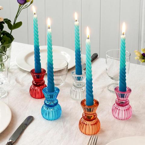 Coloured glass candle holders with blue candles on a white tablecloth