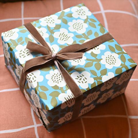 A gift wrapped in Astrid Oliver wrapping paper with a brown ribbon