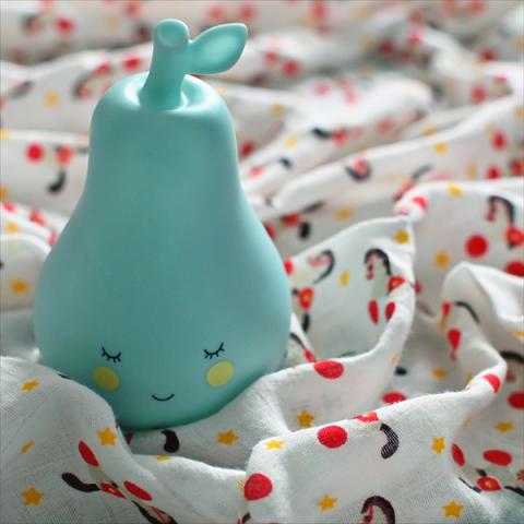 A pear night light sits on a swaddling blanket with a circus horse pattern