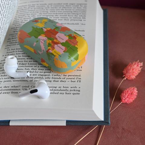 A World Map mini travel case rests on a book next to some wireless headphones