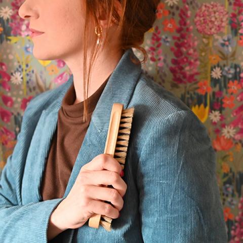 A woman brushes her coat with a wooden clothes brush