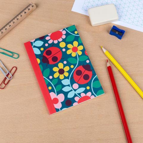 An A6 notebook with a ladybird print, on a table with pencils and paperclips