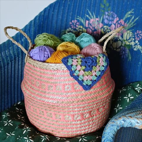A coral belly basket holding colourful balls of yarn