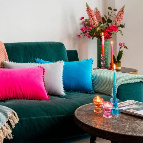 Bright cushions on a dark green sofa with colourful glass candle holders