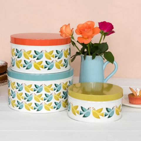 Three round cake tins with a retro bird print, next to a vase of flowers