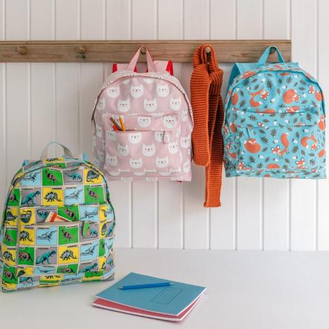 Three children's backpacks hanging up and on a table with notebooks and an orange scarf