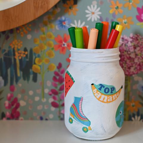 A painted jar decorated with decoupage, filled with colouring pens
