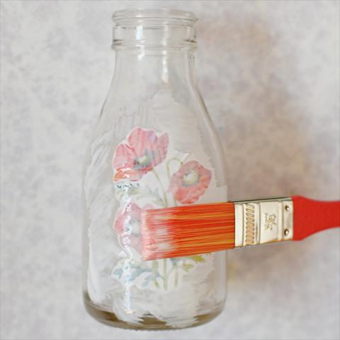 A glass bottle being painted with a layer of glue