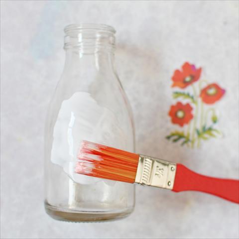 A glass bottle being painted with a layer of glue