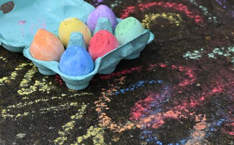 Chalk eggs in a box next to chalk drawings on the ground